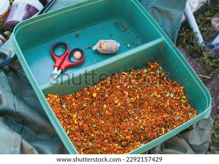 Small, sweet multicolored pieces in a plastic container. Soy pieces used as bait for carp fishing. Fragrant bait for carp fishing on carp baits. Bait for fishing in the form of small pieces. Royalty-Free Stock Photo #2292157429