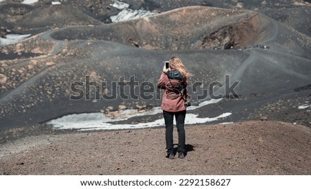 Unrecognizable girl in the mountains takes a photo of landscape. Young hiker takes pictures of volcanic terrain with her smartphone in winter. New generations and nature photography.