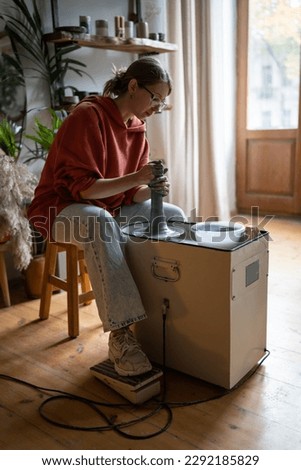 Thoughtful woman ceramist owner of art workshop shaping clay vase on potter wheel in creative studio. Interested pleased girl owner of art workshop engaged in production of porcelain tableware Royalty-Free Stock Photo #2292185829