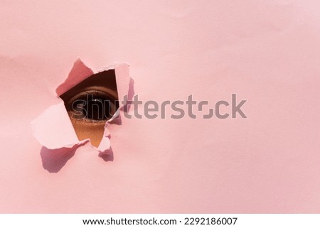 Observing the eye of a baby girl in the hole of pink paper. Eye under the pink paper.
