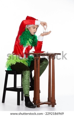 Full portrait of young girl wearing red santa clause hat like grinch question look with empty milk, isolated on white background. Human emotion facial expression