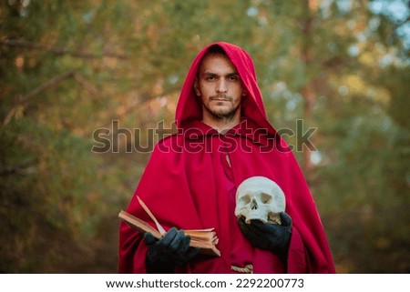 A sorcerer in red clothes with a skull and a book in his hands reads a spell. Medieval monk reads a prayer. fantasy image for halloween Royalty-Free Stock Photo #2292200773