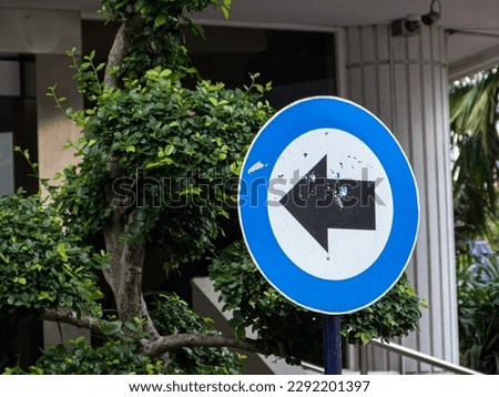 Mandatory road sign (black arrow in blue circle with white background) in front of a building in Cikini, Central Jakarta
