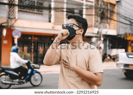 Asian young man wearing face mask to protect PM 2.5, protect pollution, anti smog and viruses on road in the city. Global warming concept. Healthcare concept. Environmental pollution concept. Royalty-Free Stock Photo #2292216925