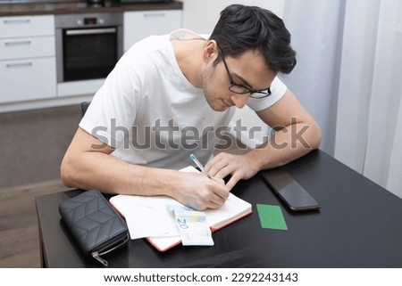 Close-up photo of man sitting at the table at home and counting his expenses from bills, invoices and credit cards