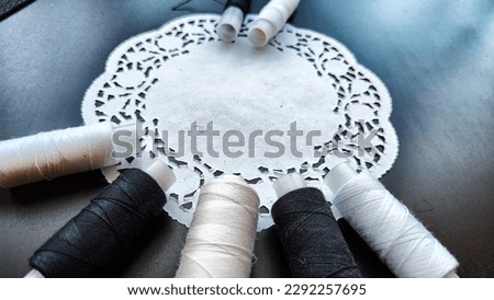 White and black spools of thread with decorative napkin on black background. Black card with abstract frame, texture and sewing threads. Top view. Partial focus