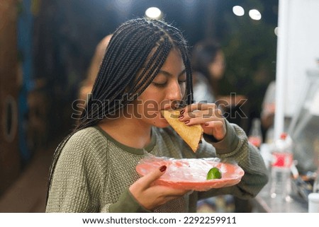 Woman eating tacos at a street mexican food stall 