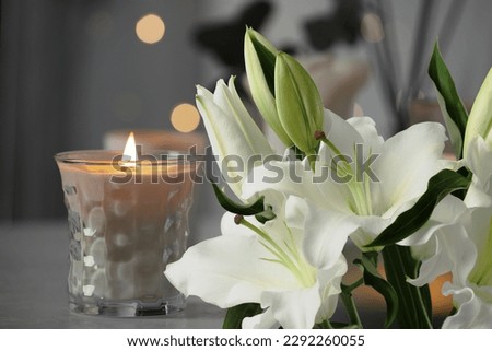 Funeral. White lilies and burning candle indoors, bokeh effect Royalty-Free Stock Photo #2292260055