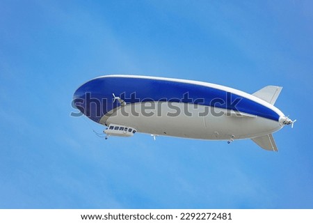 A blue and white airship with passengers on board flies against the blue sky.  Royalty-Free Stock Photo #2292272481