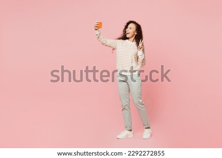 Full body young woman of African American ethnicity wear light casual clothes doing selfie shot on mobile cell phone post photo on social network show v-sign isolated on plain pastel pink background