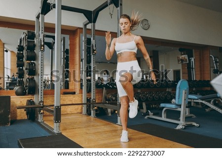 Full body young strong skinny sporty athletic sportswoman woman 20s in white sportswear jogging run in place warm up training do exercises in gym indoors. Workout sport motivation lifestyle concept Royalty-Free Stock Photo #2292273007