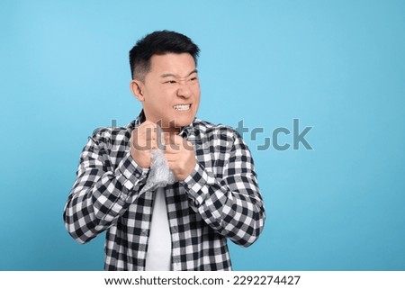 Emotional asian man with bubble wrap on light blue background. Space for text