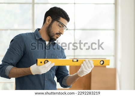 Professional male carpenter using water level meter or spirit level tool in wood workshop. Asian male joiner working in furniture workshop. SME, Start up and small business concept Royalty-Free Stock Photo #2292283219