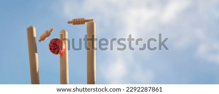 Cricket ball hitting wicket stumps knocking bails out against blue sky background Royalty-Free Stock Photo #2292287861