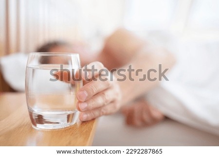 Glass of fresh drinking water on bed bedside table man thirsty reaching hand Royalty-Free Stock Photo #2292287865