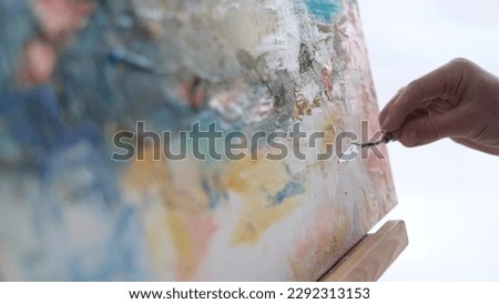 An artist in a work coat records a video blog as he paints a picture with brushes on a white canvas. The process of creating an oil painting in the workshop. 