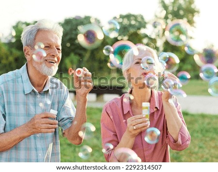 Happy active senior couple having fun blowing soap bubbles in park outdoors. Vitality and active senior couple concept
