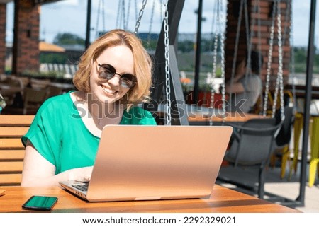 Happy smiling girl in sunglasses using application on digital laptop in a street cafe. Girl student working remotely, using a laptop or shopping online. Distance learning, online education