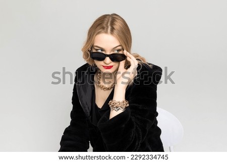 Young Curly blonde girl elegantly dressed, with a bright red lipstick on the lips and a black sunglasses. expensive clothes, style and fashion concept.