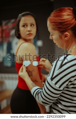 Tattoo artistwith red hair  looking at the two sizes of the tattoo design on her client