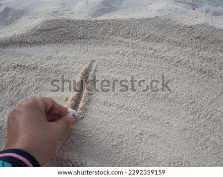 The left hand uses a broken coral to write letter L or number 1 or straight line in wet sand. People often write messages or draw picture in sand to communicate or send a message to someone.