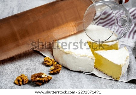 composition from rose wine bottle,glass, round cheese with one cut slice,walnuts,cork and corkscrew on kitchen striped towel or gray background tiles imitation.bottle upside down,flat lay front view