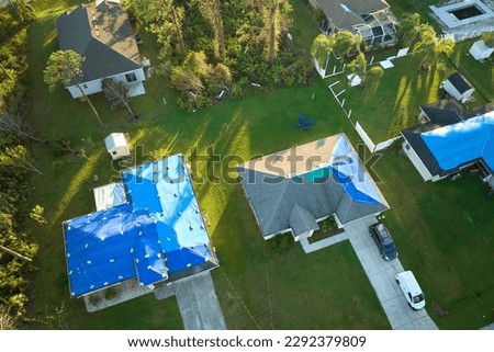 Top view of leaking house roofs covered with protective tarp sheets against rain water leaks until replacement of asphalt shingles. Damage of building rooftop as aftermath of hurricane Ian in Florida Royalty-Free Stock Photo #2292379809