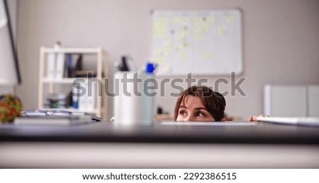 Scared Woman Hiding Behind Chair And Under Desk Royalty-Free Stock Photo #2292386515
