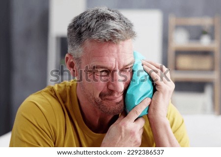 Upset Man Touching Cheek With Cold Water Bag At Home Royalty-Free Stock Photo #2292386537