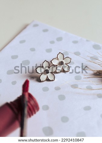 Composition with female accessories. A pair of small flower  earrings and a lipstick on polka dot background. Vintage fashion concept and minimalist style. Spring mockup. Top view.