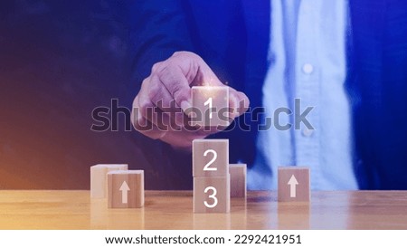 Businessman hand puts a wooden block with the number one on top of the tiered cubes. First step, Level or Ranking and Business competition concept. Royalty-Free Stock Photo #2292421951