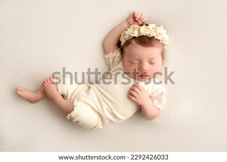 A cute little newborn baby in a white suit and a headband with flowers on his head sleeps sweetly. Professional macro photo on a white background.
