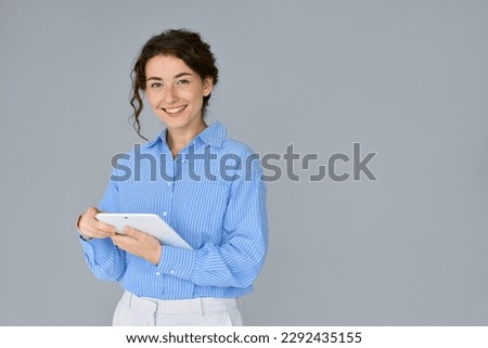 Young happy professional business woman office worker holding digital tablet, using tab computer standing isolated at grey background advertising online education on smart tech device.
