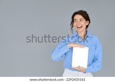 Happy smiling business woman holding digital tablet computer showing blank empty mock up screen looking aside advertising software, website or web service standing isolated on gray background.
