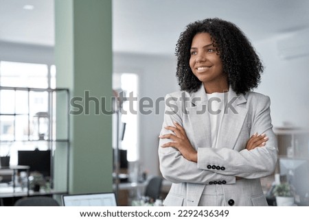 Happy smiling portrait of young African American leader manager, stands confident, crossed arms and looking aside in business office center. Portrait of professional business woman in stylish suit. Royalty-Free Stock Photo #2292436349