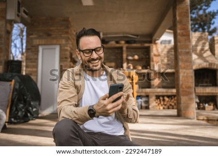 One man caucasian male with beard and eyeglasses sit outdoor in sunny day wear shirt use mobile smart phone for sms text messages browse internet online or video call use app copy space real people Royalty-Free Stock Photo #2292447189