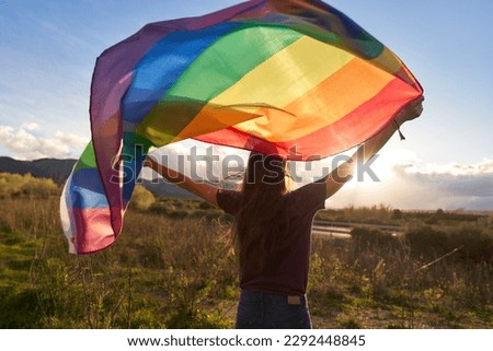 Non-binary person waving LGTB flag in the meadow Royalty-Free Stock Photo #2292448845