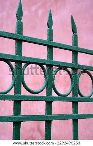 An old forged, metal fence with pikes, pins, rings from Soviet times painted with green paint.