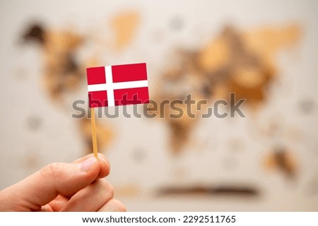 Denmark flag in mans hand on the wooden world map background. Global economy and geopolitics concept. 