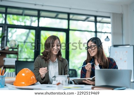 Concept of engineering consulting, Two female engineers discussing about model of building together; Two female architects are studying blueprint of building house.