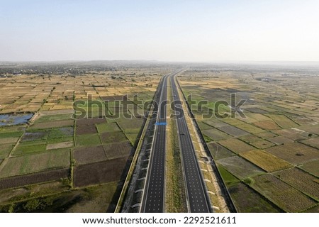 orbit aerial drone shot of new delhi mumbai jaipur express elevated highway showing six lane road with green feilds with rectangular farms on the sides Royalty-Free Stock Photo #2292521611
