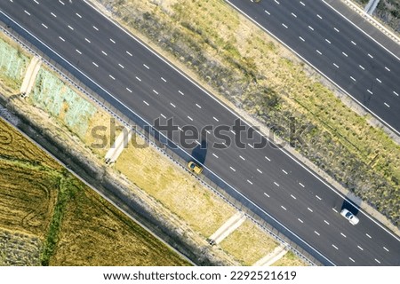 aerial drone shot moving along and shooting straight down of new delhi mumbai jaipur express elevated highway showing six lane road with green feilds with rectangular farms on the sides Royalty-Free Stock Photo #2292521619