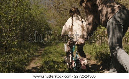 mother teaches little child ride bike road park. happy family concept. outdoor cycling. child kid pedals two-wheeled bicycle walk. mom parent rides girl daughter children bike. family vacation outdoor