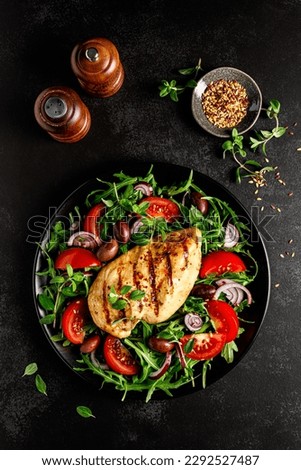 Chicken breast fillet grilled and fresh vegetable green salad with arugula, tomatoes and olives on black background, healthy food, mediterranean diet, top view Royalty-Free Stock Photo #2292527487