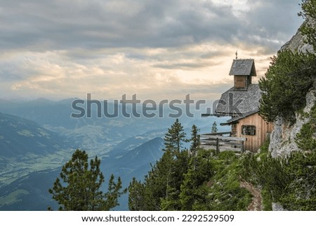 View on a charming small mountain chapel built on the edge of a mountain cliff overlooking the valley in the austrian Alps on Stoderzinken mountain. Dachstein mountains. Royalty-Free Stock Photo #2292529509
