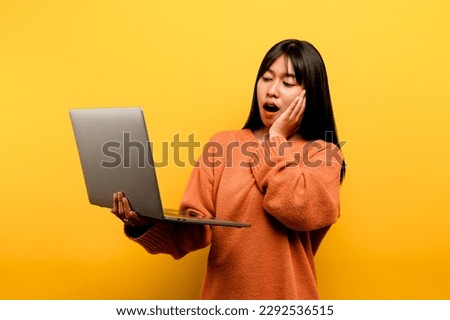 online communication concept asian girl use laptop at home yellow studio photo She is happy to spend her free time online while chatting with friends on social networks, shopping or working online.