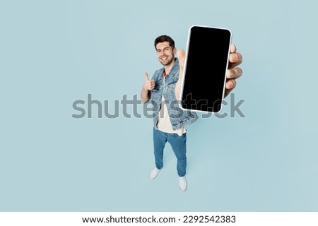 Full body top view young man he wear denim vest red t-shirt casual clothes hold in hand use close up mobile cell phone with blank screen workspace area isolated on plain light blue background studio