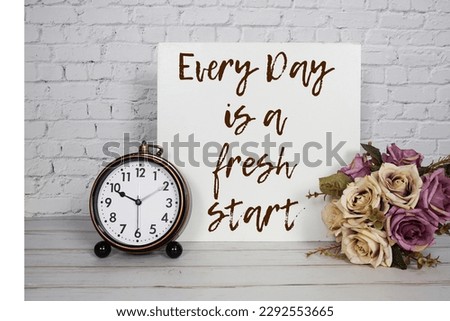 Every Day is a fresh start text message with alarm clock and flower bouquet on white brick wall background