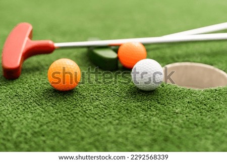 Mini-golf clubs and balls of different colors laid on artificial grass. Royalty-Free Stock Photo #2292568339