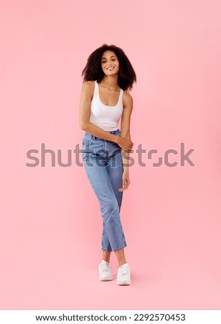 Full body length portrait of young african american lady with curly hair posing in casual wear over pink studio background, vertical shot, cropped